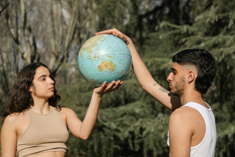 A man and woman hold a globe together in an outdoor setting, symbolizing unity.